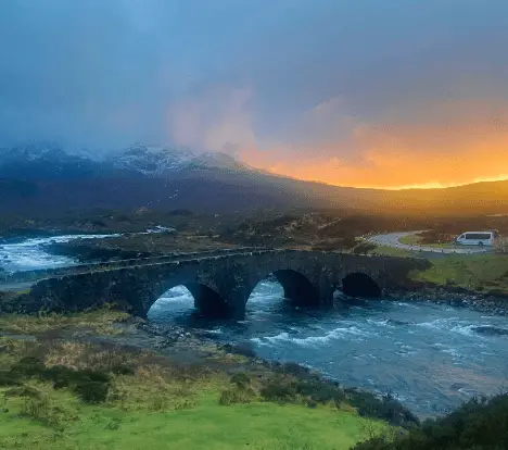 Old stone bridge going over river, mountains int he background. The sun is setting.Glens in Scotland