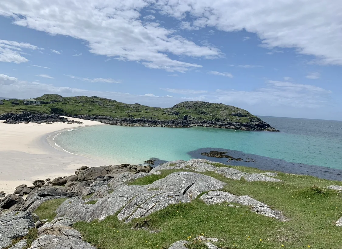 Achmelvich Bay Hpto of Achmelvich Bay, water is blue and thee are grey rock surrounding the beach.