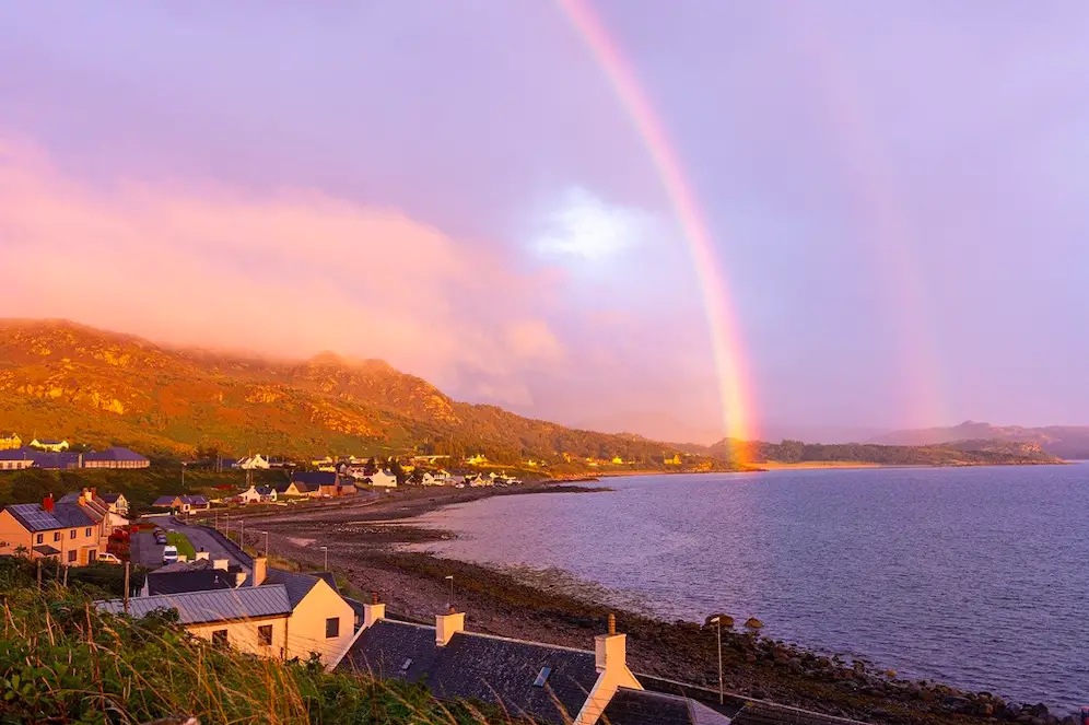 Gairloch, houses lined up along the coast of water. With a rainbow coming out of the water and across the sky.