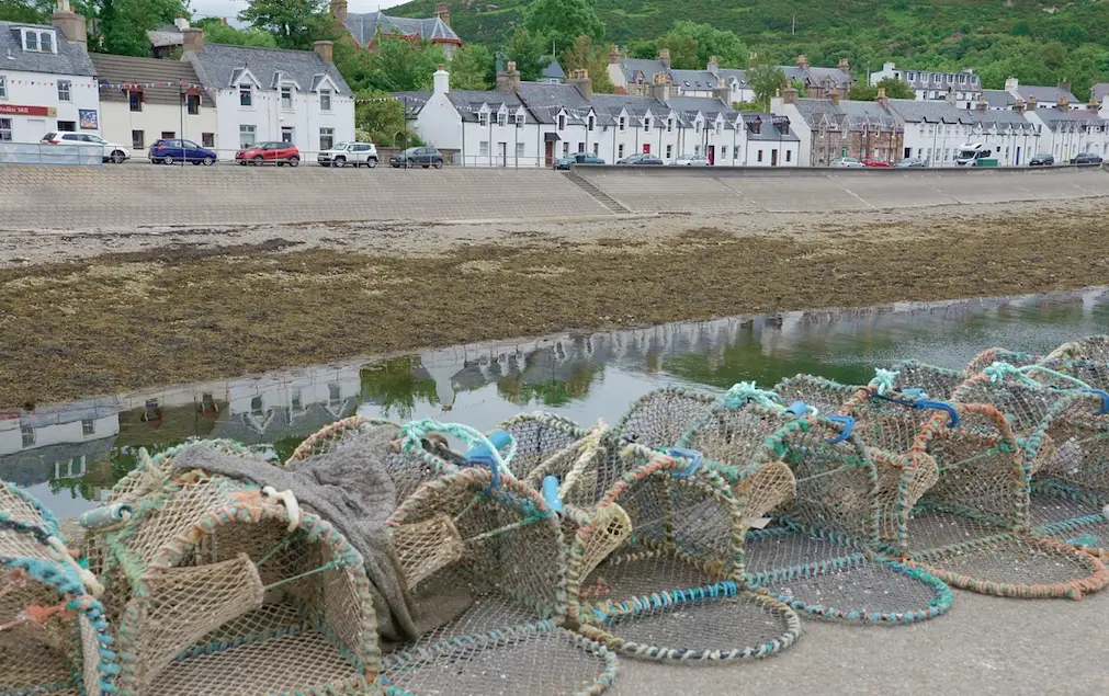 Row of white houses in the background, sand in the middleground and fishing equipment in the foreground.