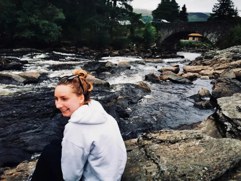 Girl sitting next to waterfall rapids