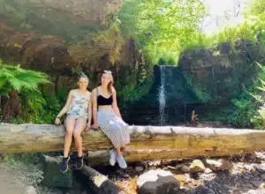 Two girls sitting on a log in front of waterfall