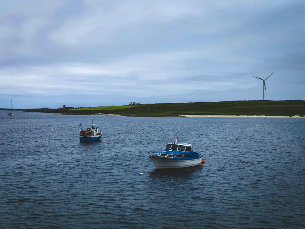 Orkney isle, boats and water in the foreground. Beach and wind turbine in the background. 