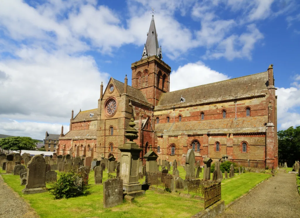 Photo of St Magnus Cathedral on a sunny day. Graveyard in foreground.